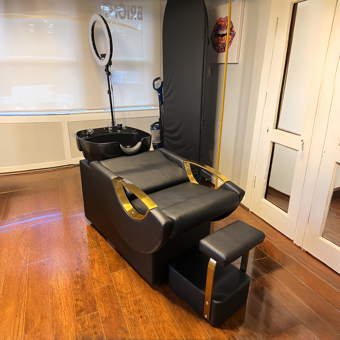 Black and gold salon backwash unit with a sink and mirror in a room with wooden flooring.