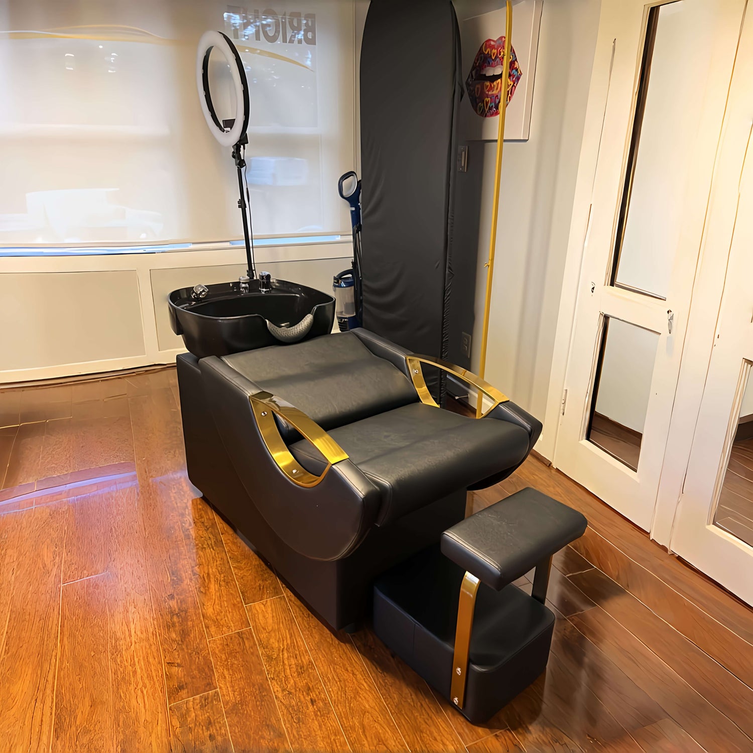 Black and gold salon backwash unit with a sink and mirror in a room with wooden flooring.