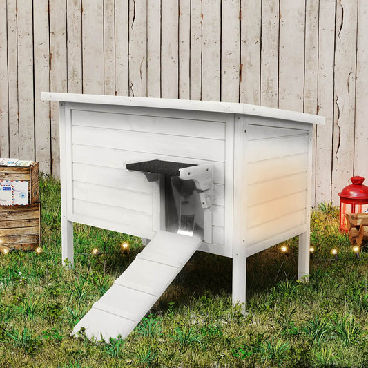 White wooden pet house with a ramp in a grassy area with a wooden fence background