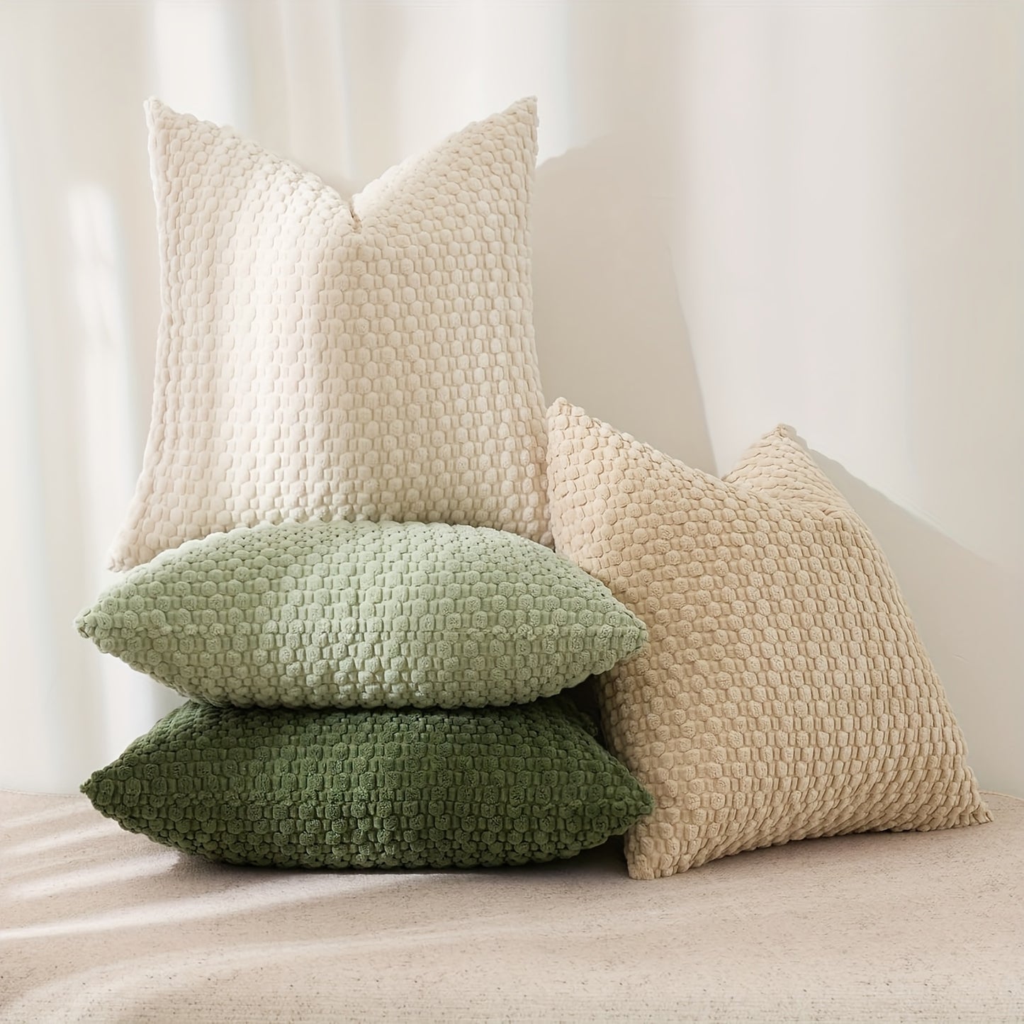 Stack of textured pillows in beige, green, and brown on a neutral background