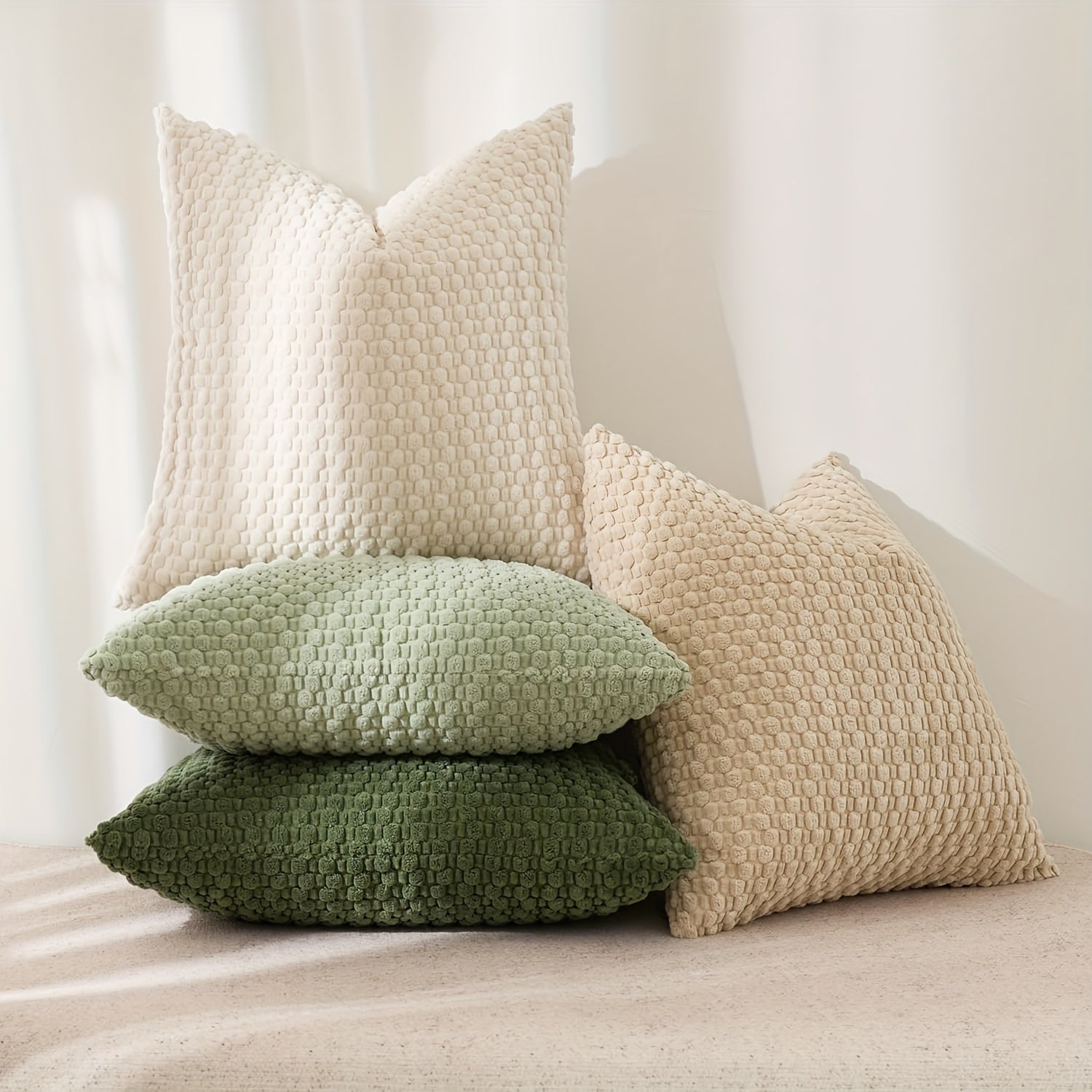 Stack of textured pillows in beige, green, and brown on a neutral background