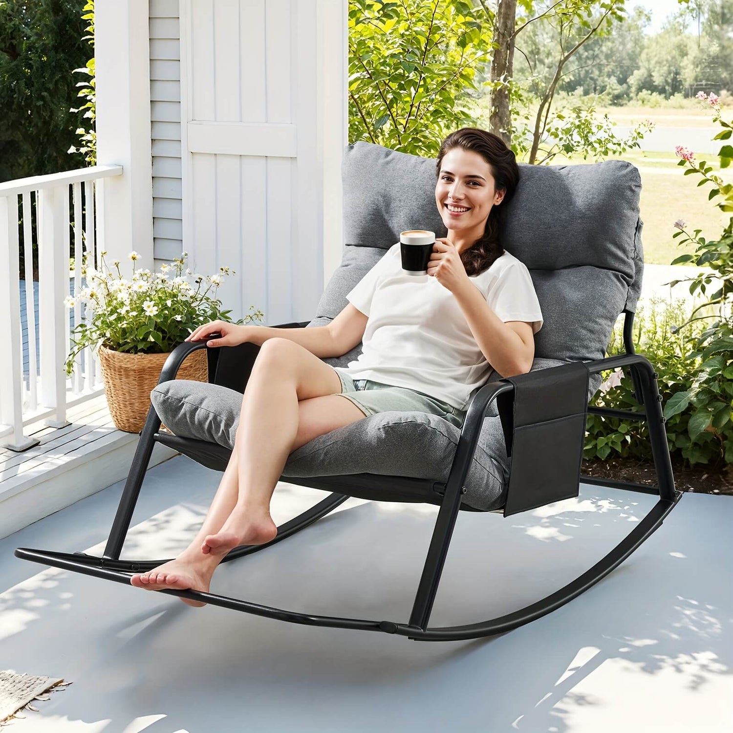 Woman sitting in a gray outdoor rocking chair on a porch, holding a cup.