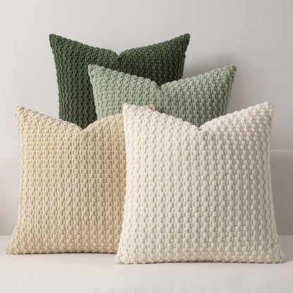 Four textured pillows in green, beige, and white on a light gray background