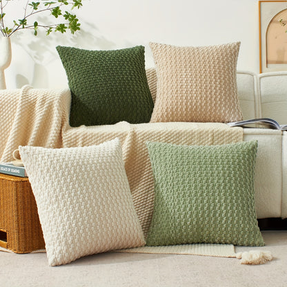 Knitted pillows in green and beige on a sofa with a woven basket and plant in the background.