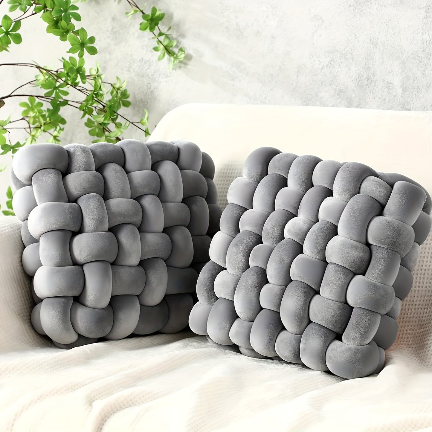 Two gray woven pillow covers on a white couch with a plant in the background.