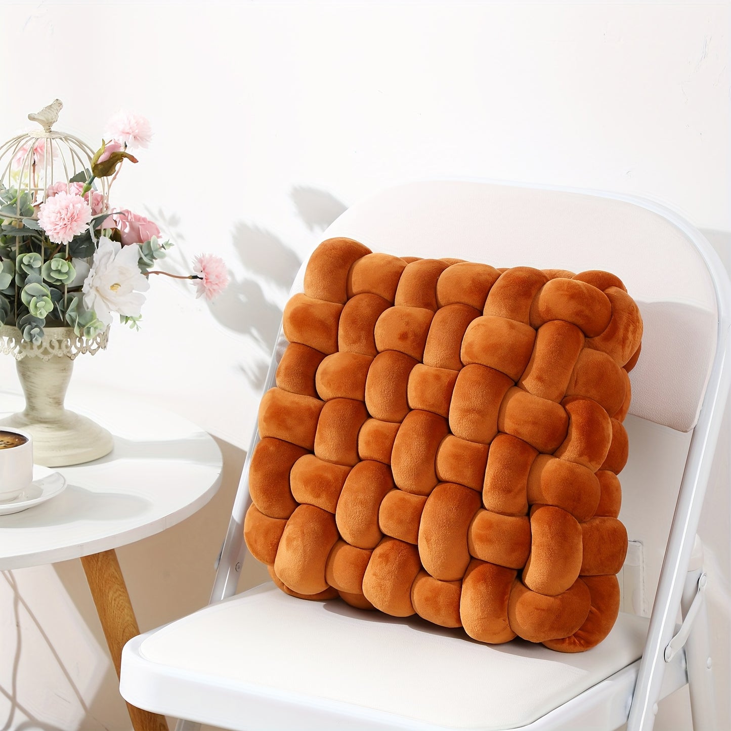 Brown textured cushion on a white chair with a decorative table and flowers in the background