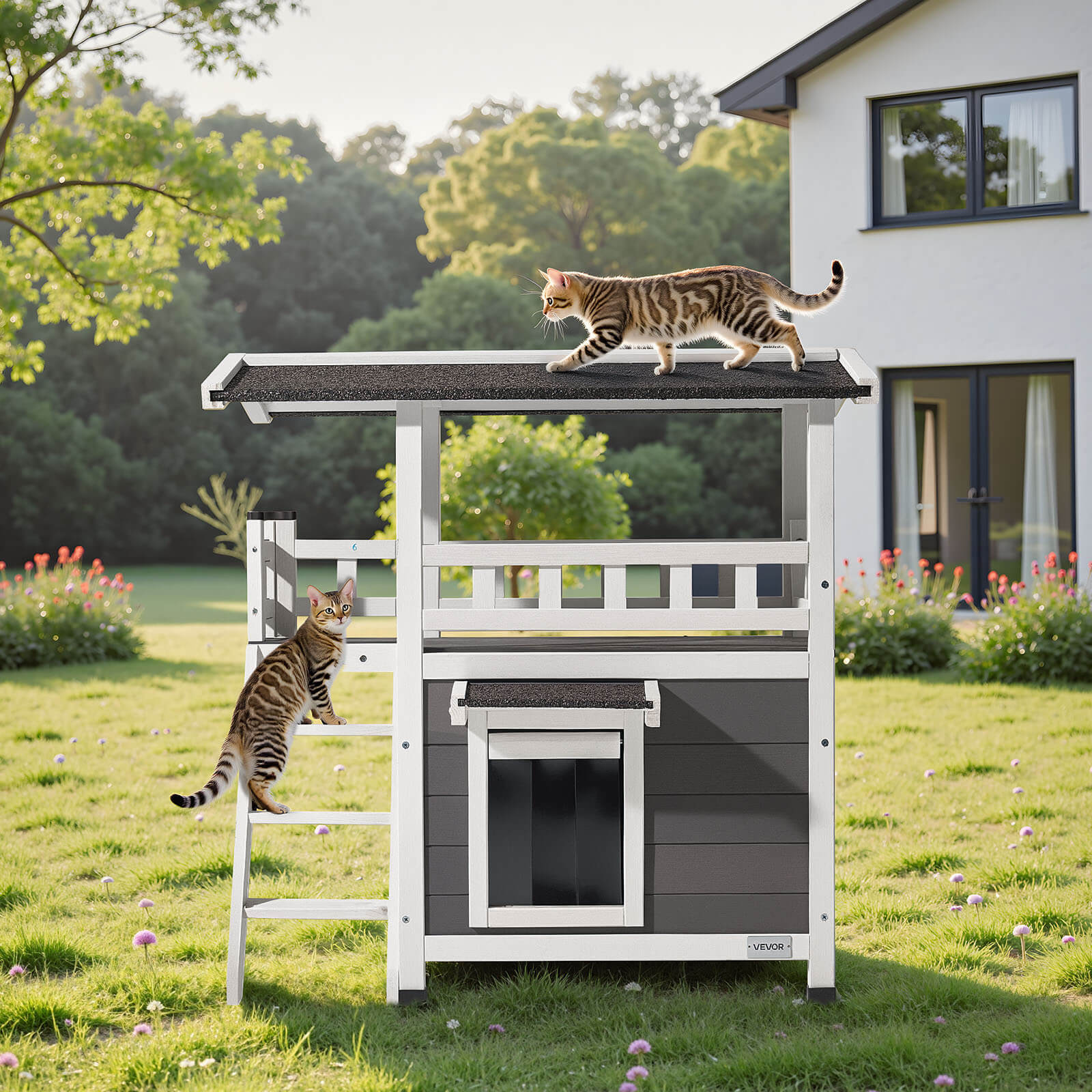 Two cats on a gray and white outdoor cat house with a house in the background.