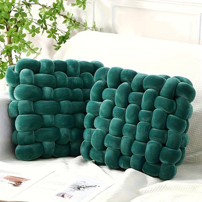 Two knot pillows on a white surface with a plant in the background