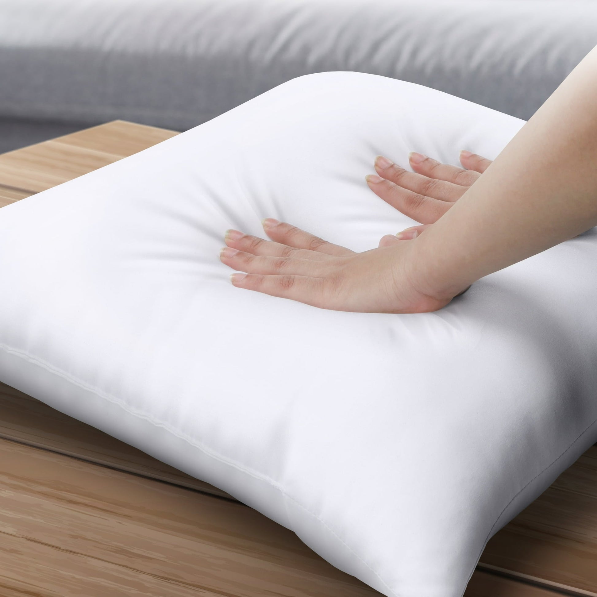 White pillow on a wooden surface with a hand touching it