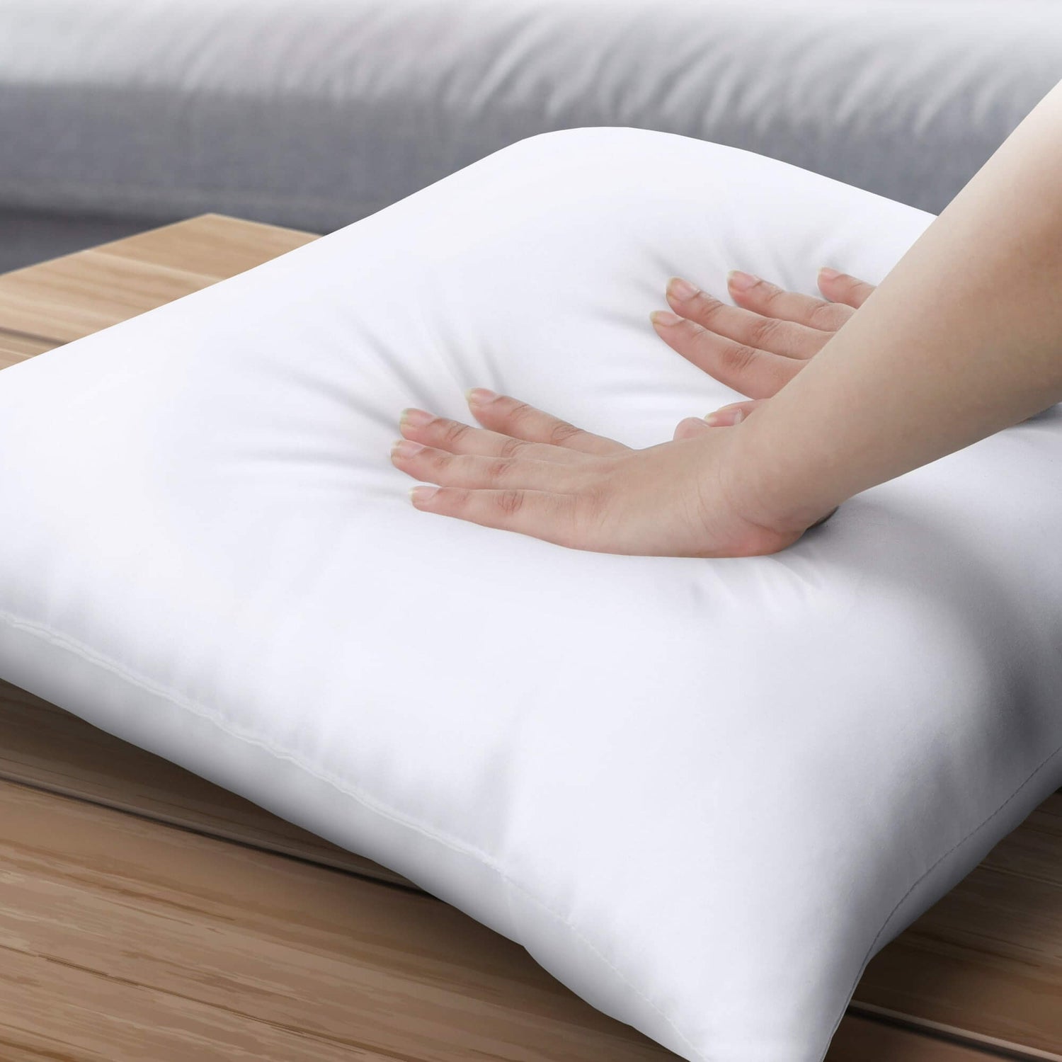 White pillow inserts on a wooden surface with a hand touching it