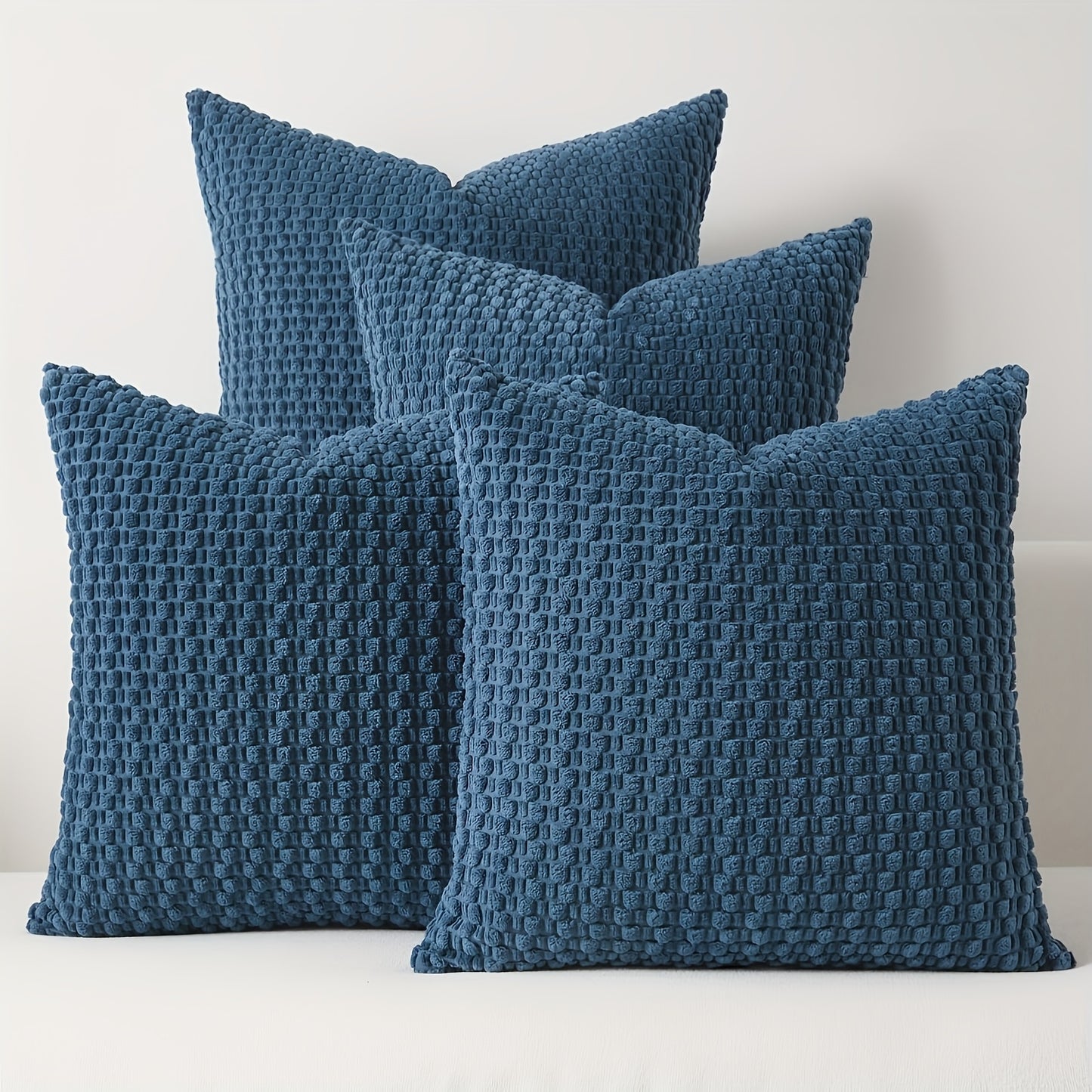 Four blue textured pillows on a white surface with a light gray background