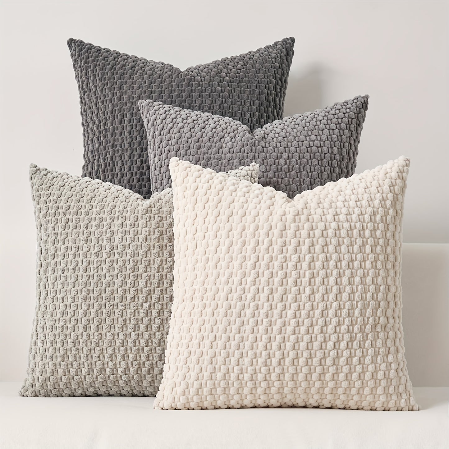 Four textured pillows in gray and white on a light background
