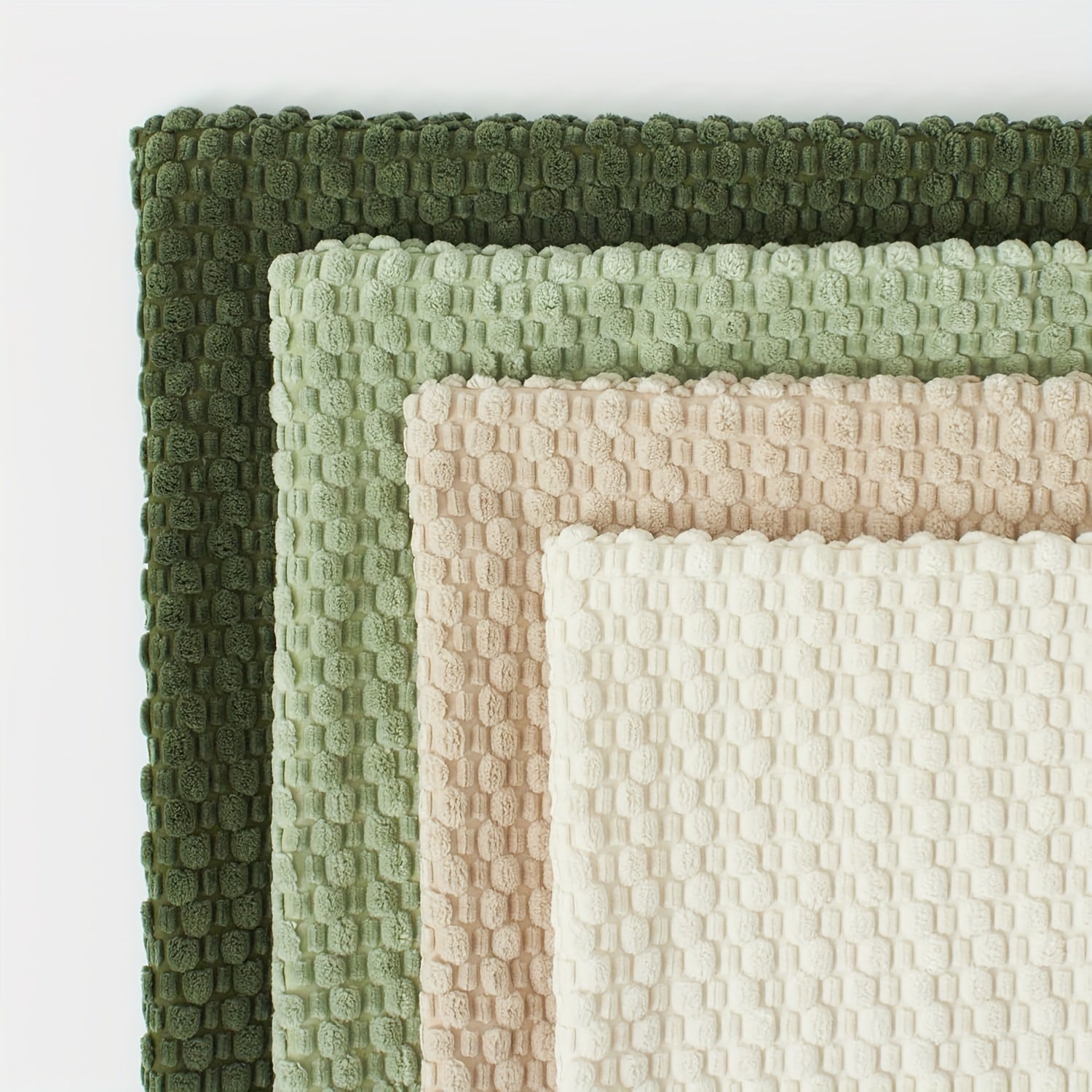 Set of textured bath mats in green, beige, and white on a white background