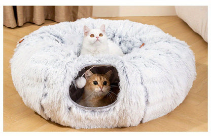 Two cats inside a fluffy white cat donut on a wooden floor.