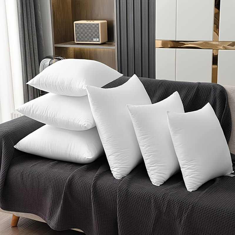 White pillows on a dark gray sofa in a room with curtains and a shelf.