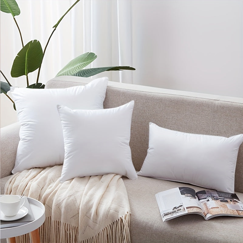 White pillows on a beige sofa with a plant and magazine in the background