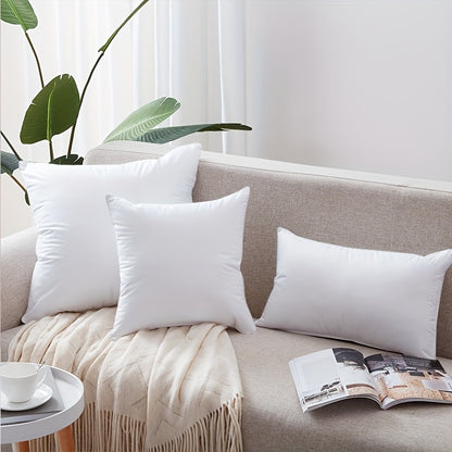 White pillows on a beige sofa with a plant and magazine in the background