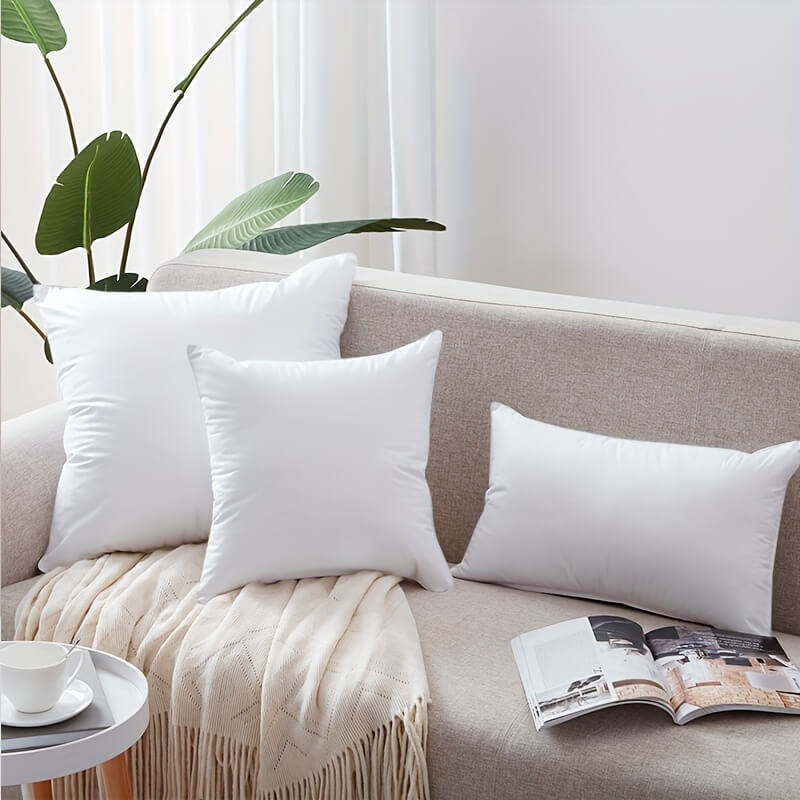 White pillows on a beige sofa with a plant and magazine in the background