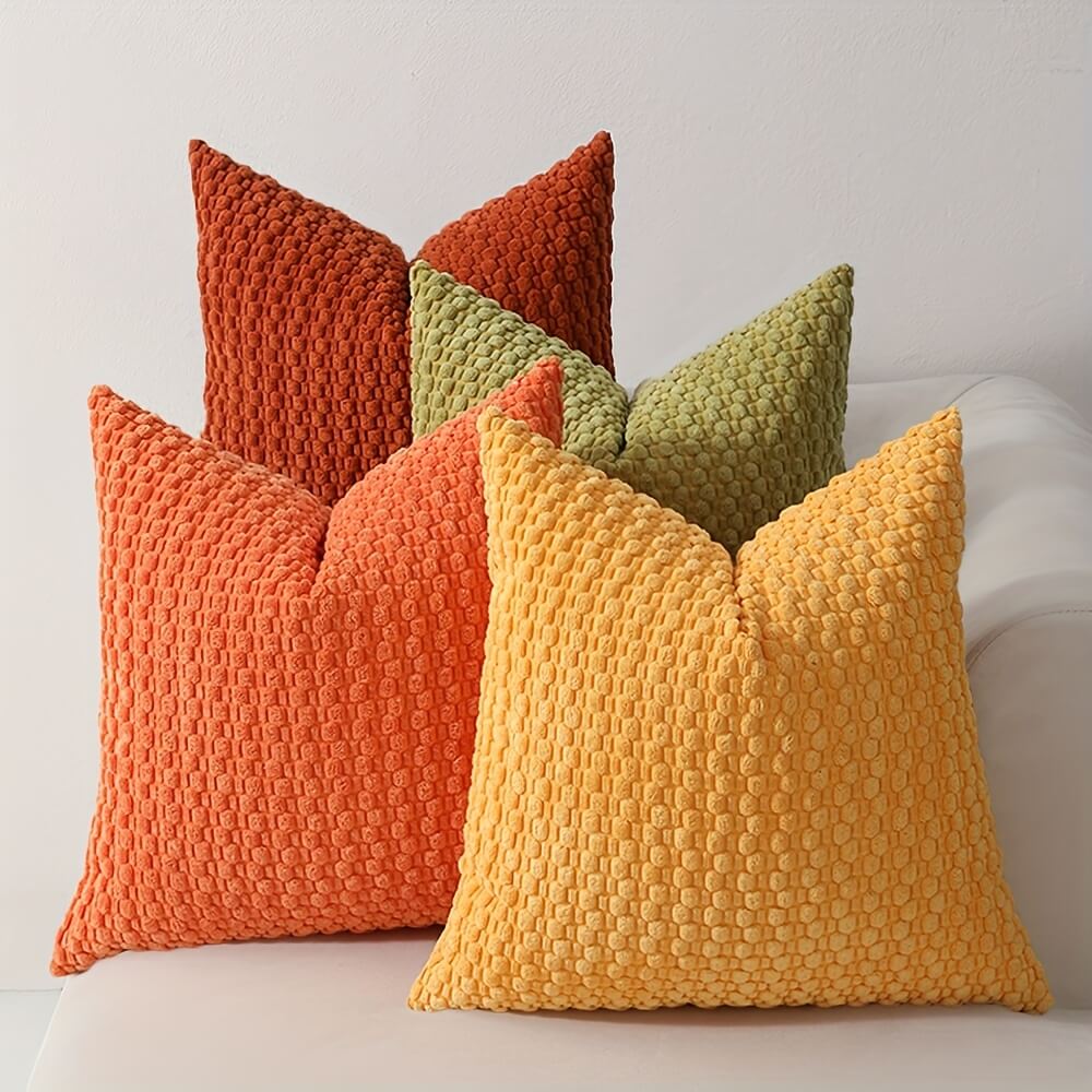 Four textured pillows in orange, green, and yellow on a white surface.