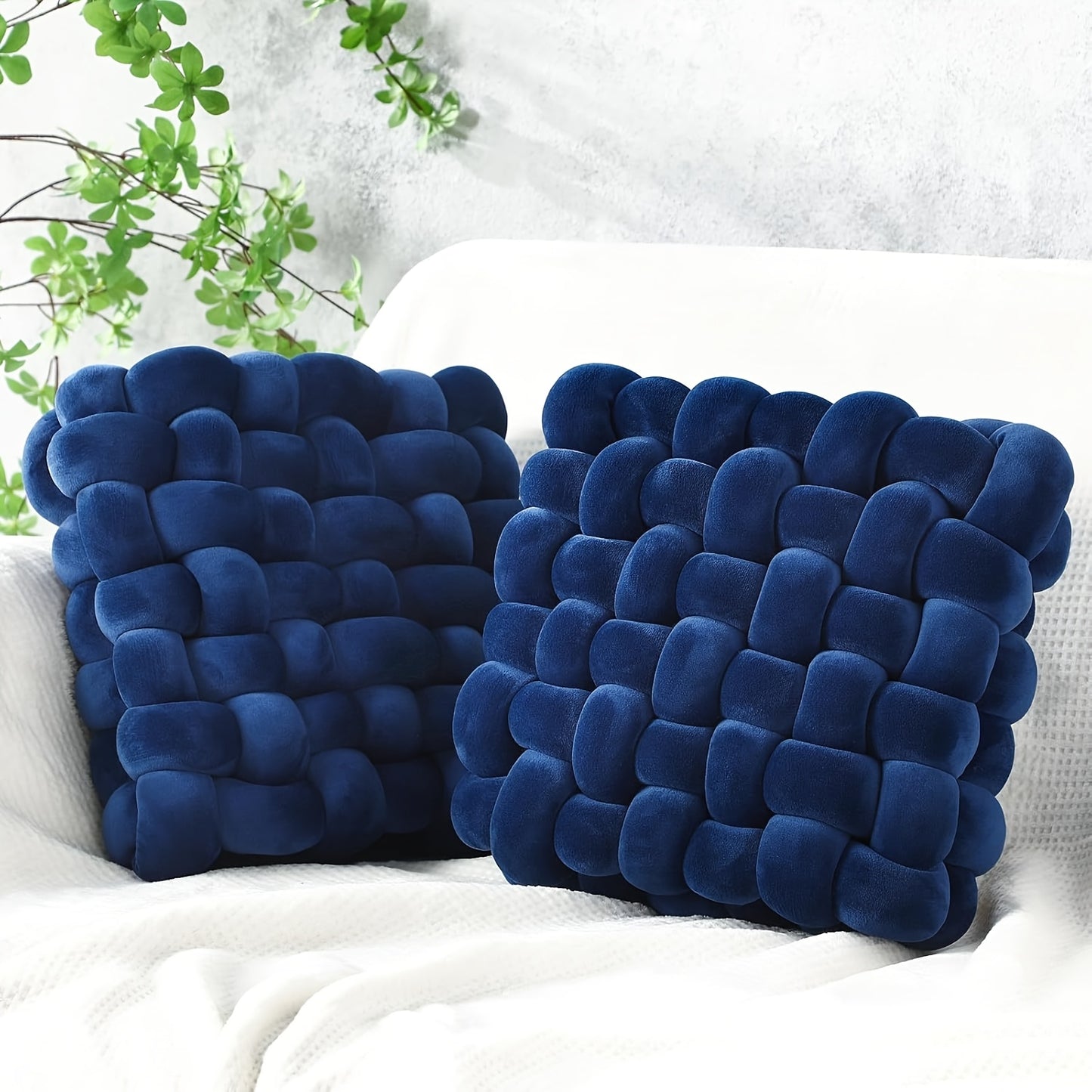 Two blue textured pillows on a white surface with greenery in the background