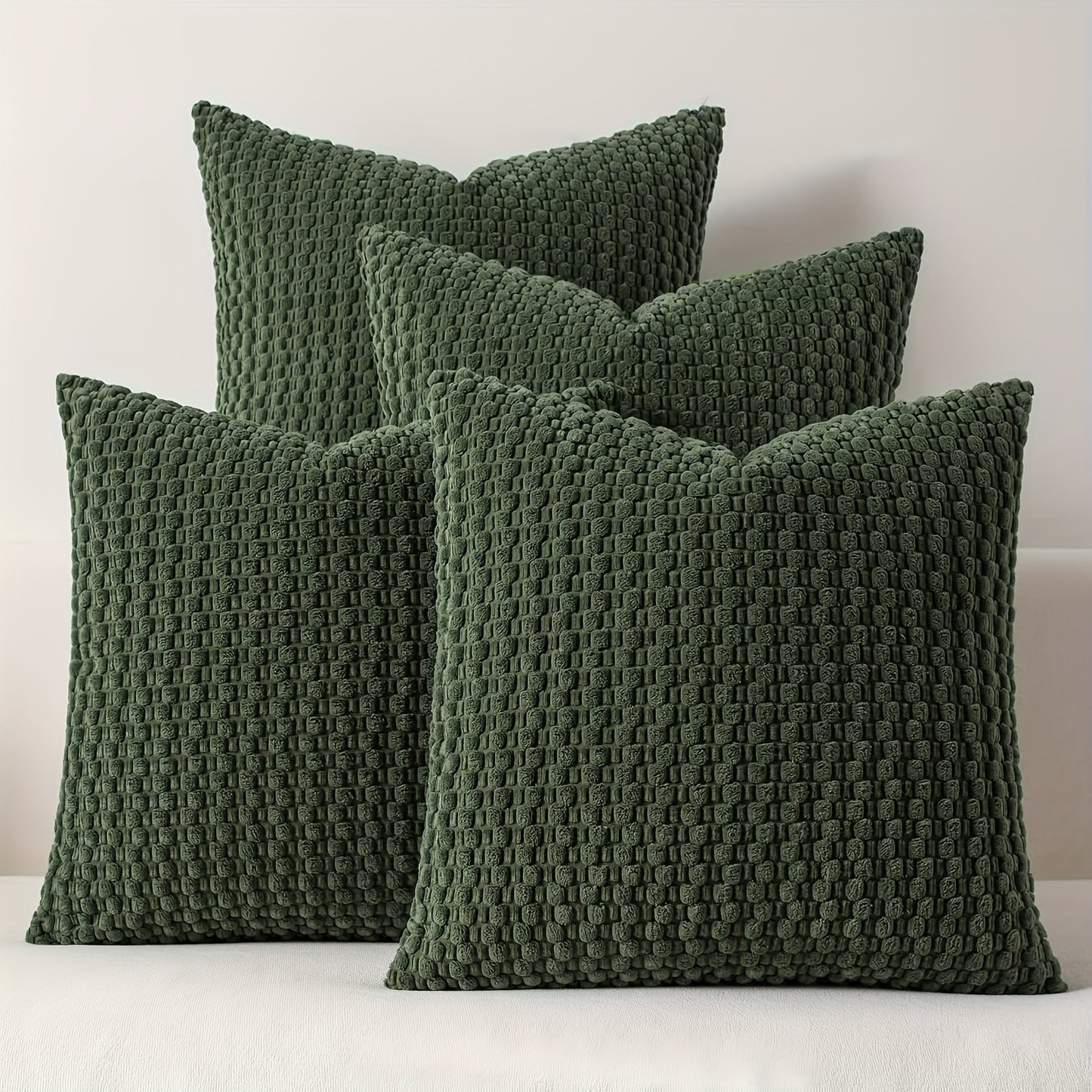 Four green textured pillows on a white surface with a light gray background
