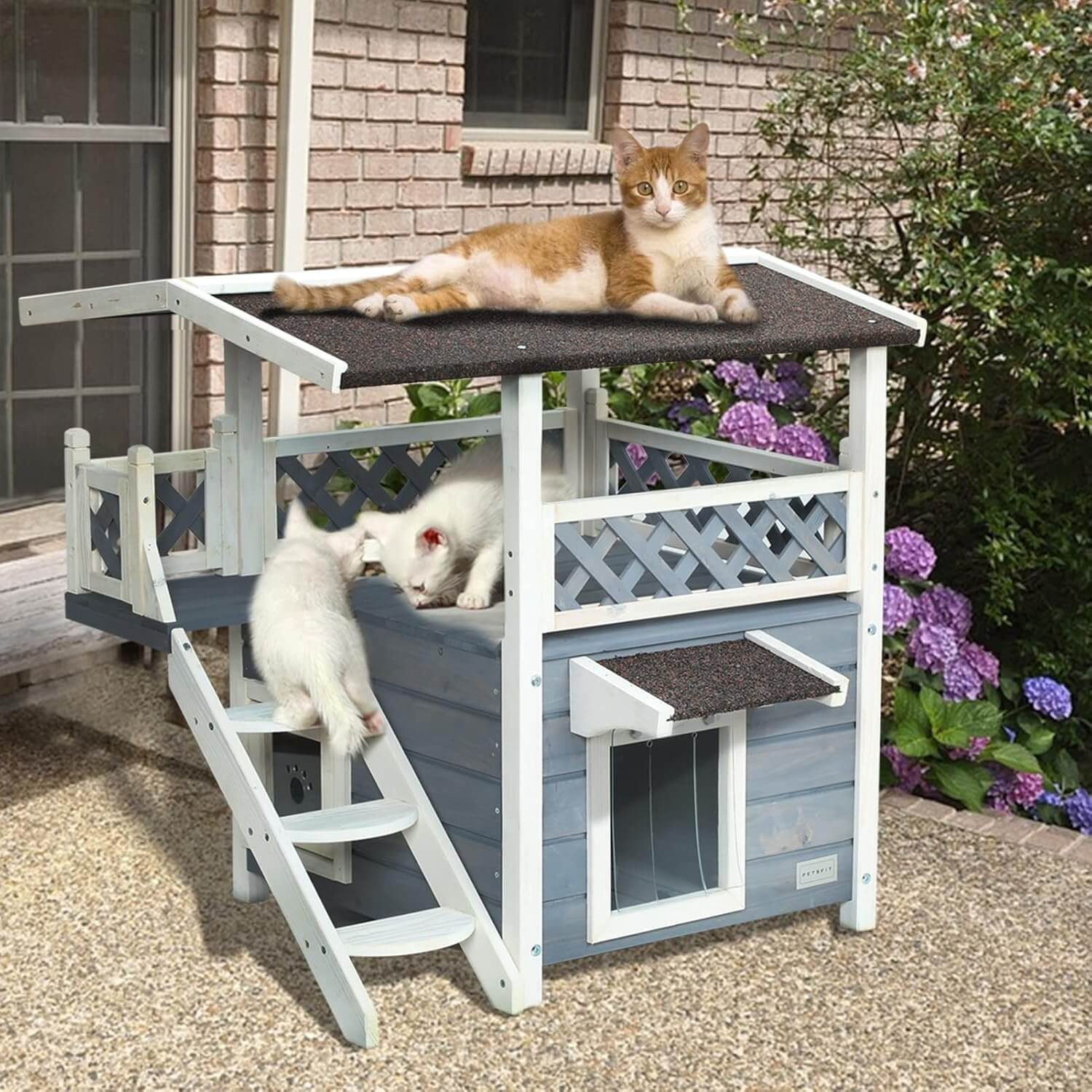 Two cats on a multi-level cat house with a staircase in an outdoor setting.