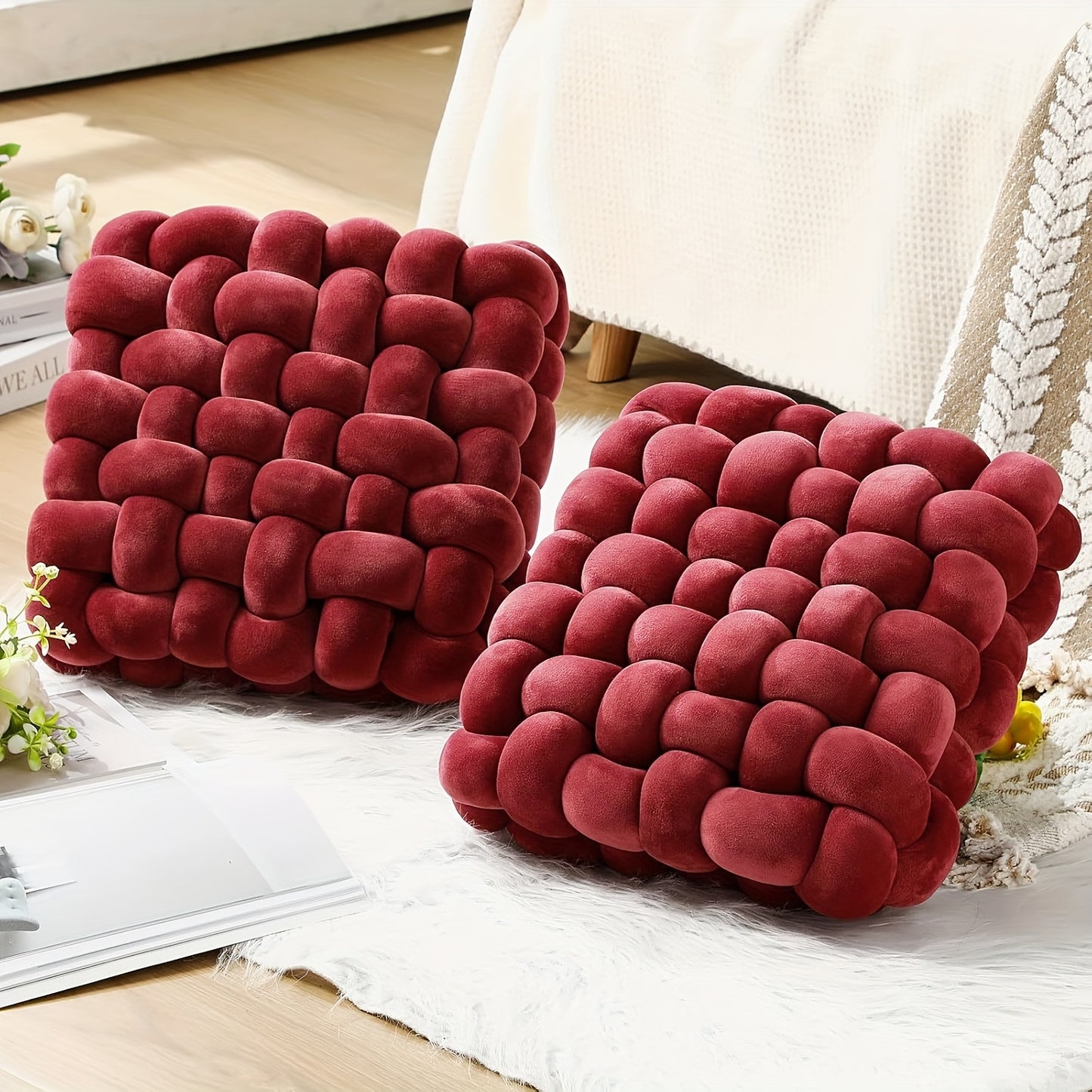 Two red braided cushions on a white surface with a blurred background