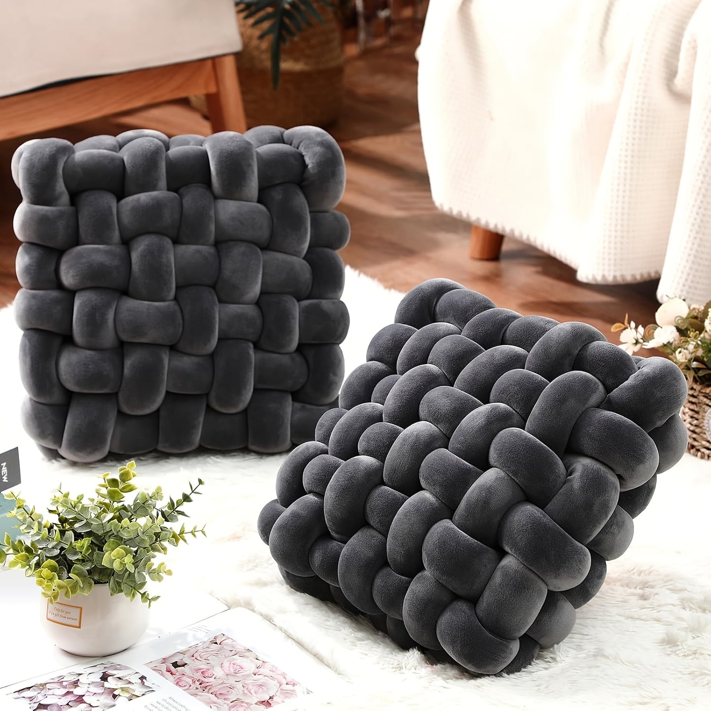 Two gray textured cube pillows on a light-colored rug with a plant and magazine in the background.