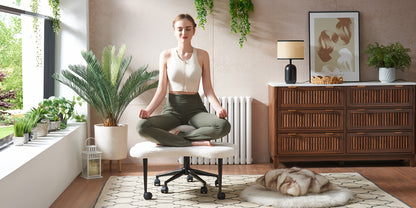 Woman meditating on a chair in a modern living room with plants and furniture.