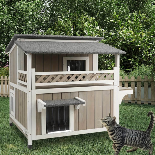 Wooden cat house with a gray roof on grass, surrounded by greenery