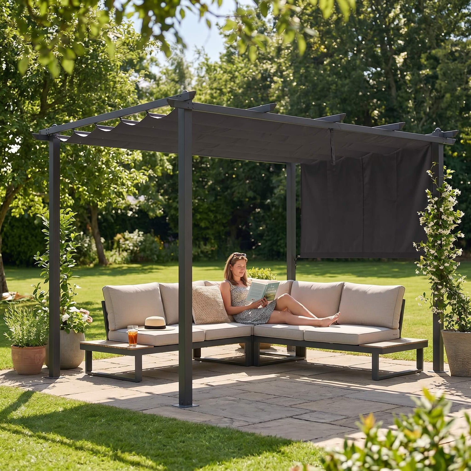 A woman reading a book while lying on a garden sectional sofa under the Aluminum Pergola with Retractable Roof in a sunny day.