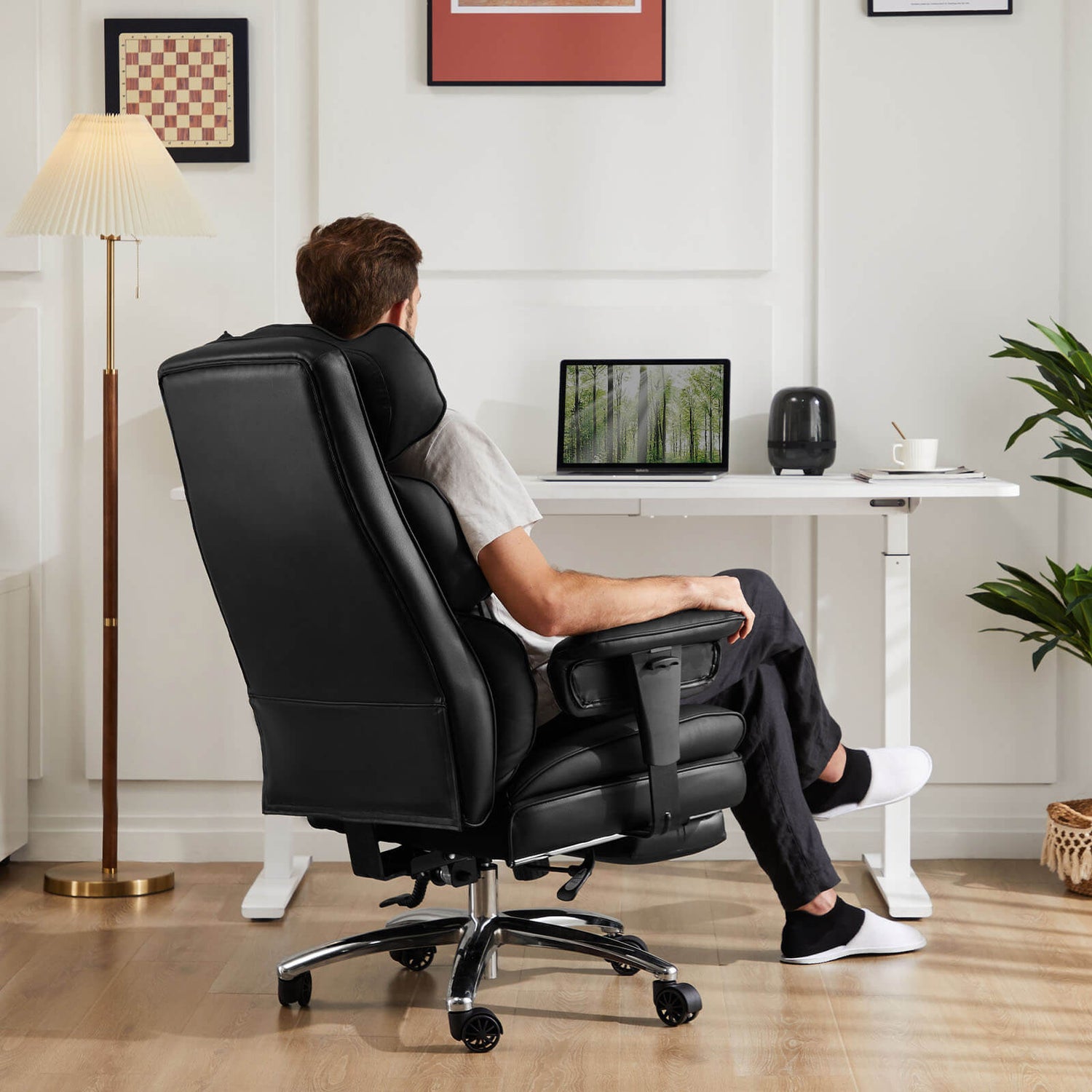 A man in his home workstation, working on his laptop computer while sitting on a black executive office chair 