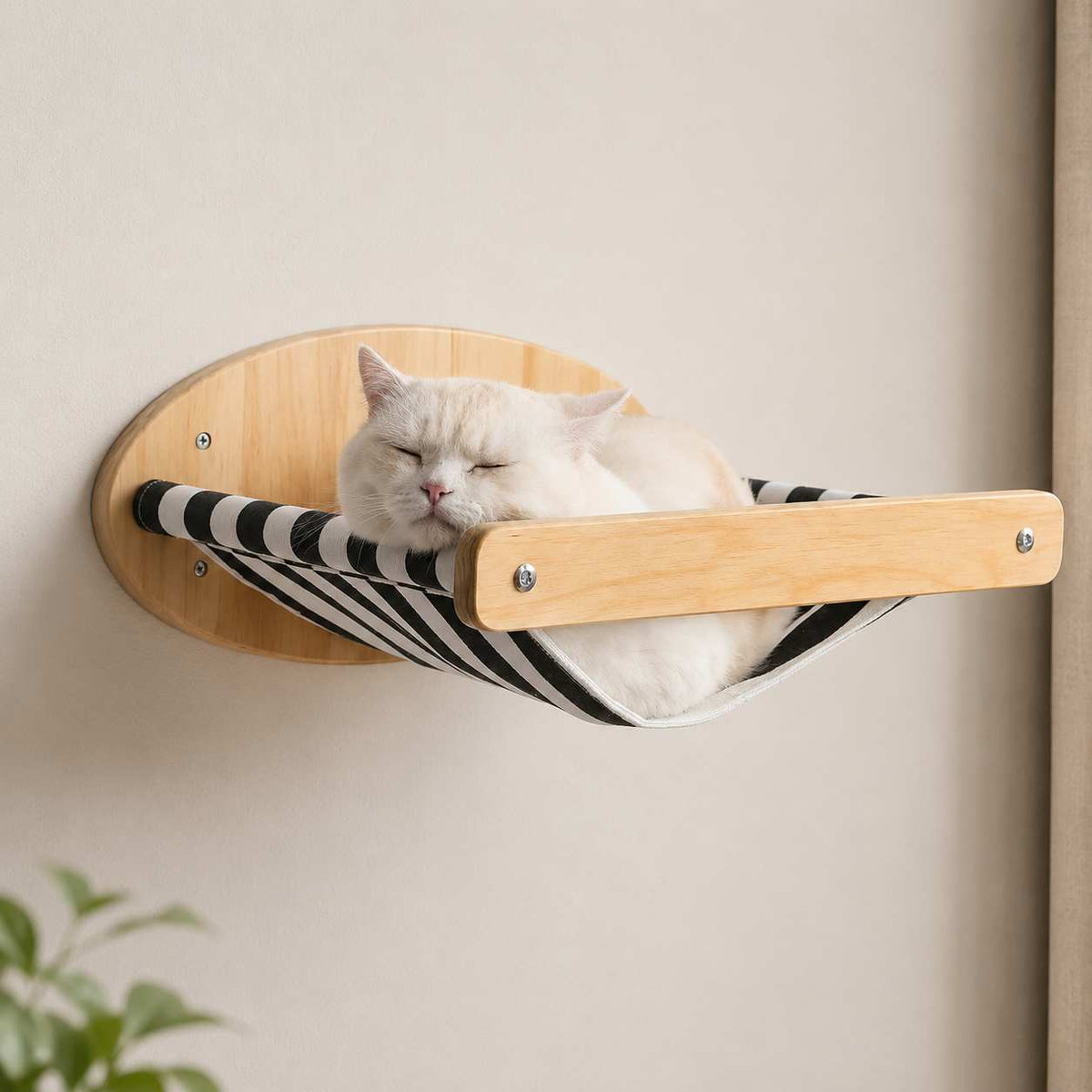 A white cat sleeping comfortably in a black and white striped wall-mounted hammock with a light wood frame, attached to a beige wall.
