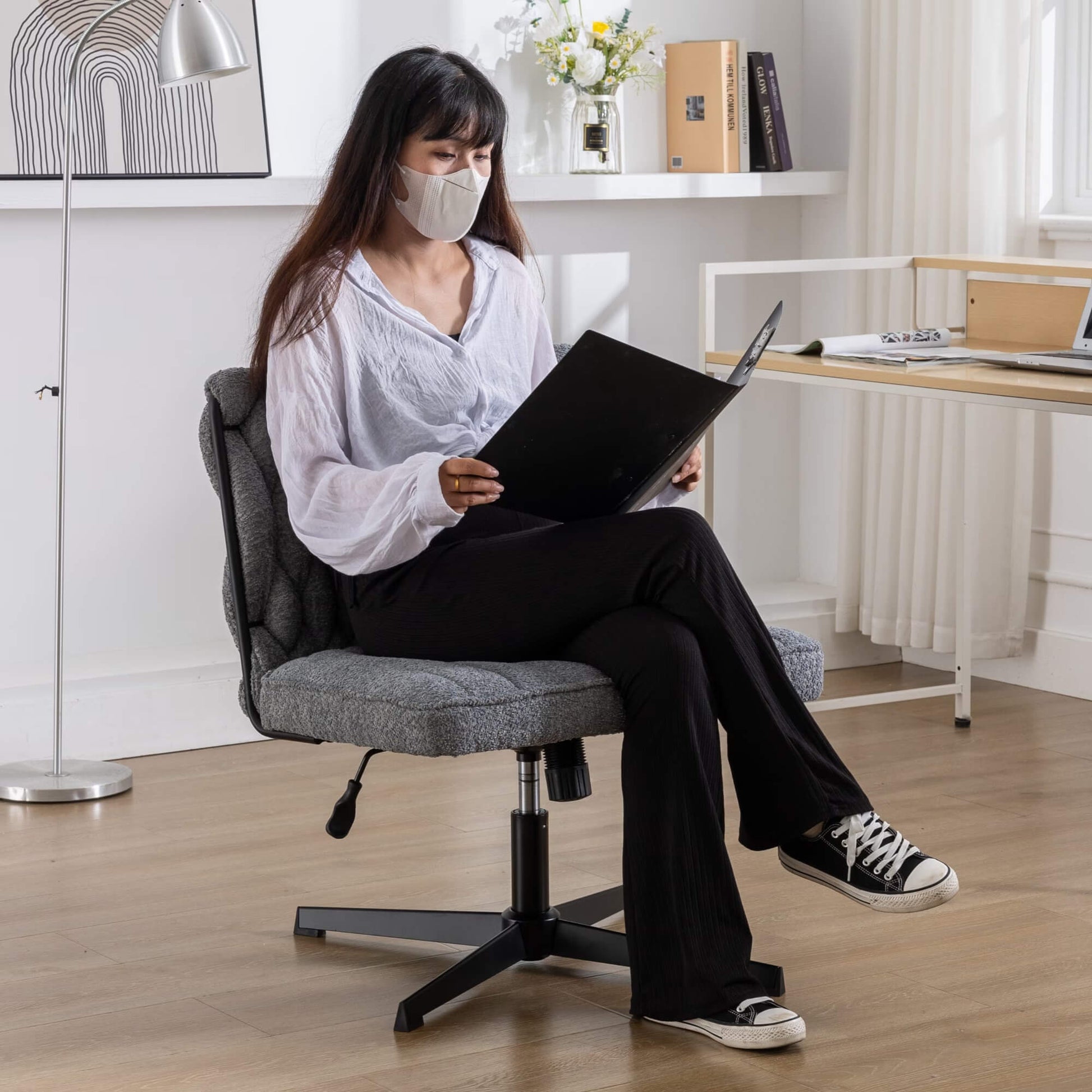 A woman working on her laptop while wearing a face mask and sitting cross legged on a fabric office chair
