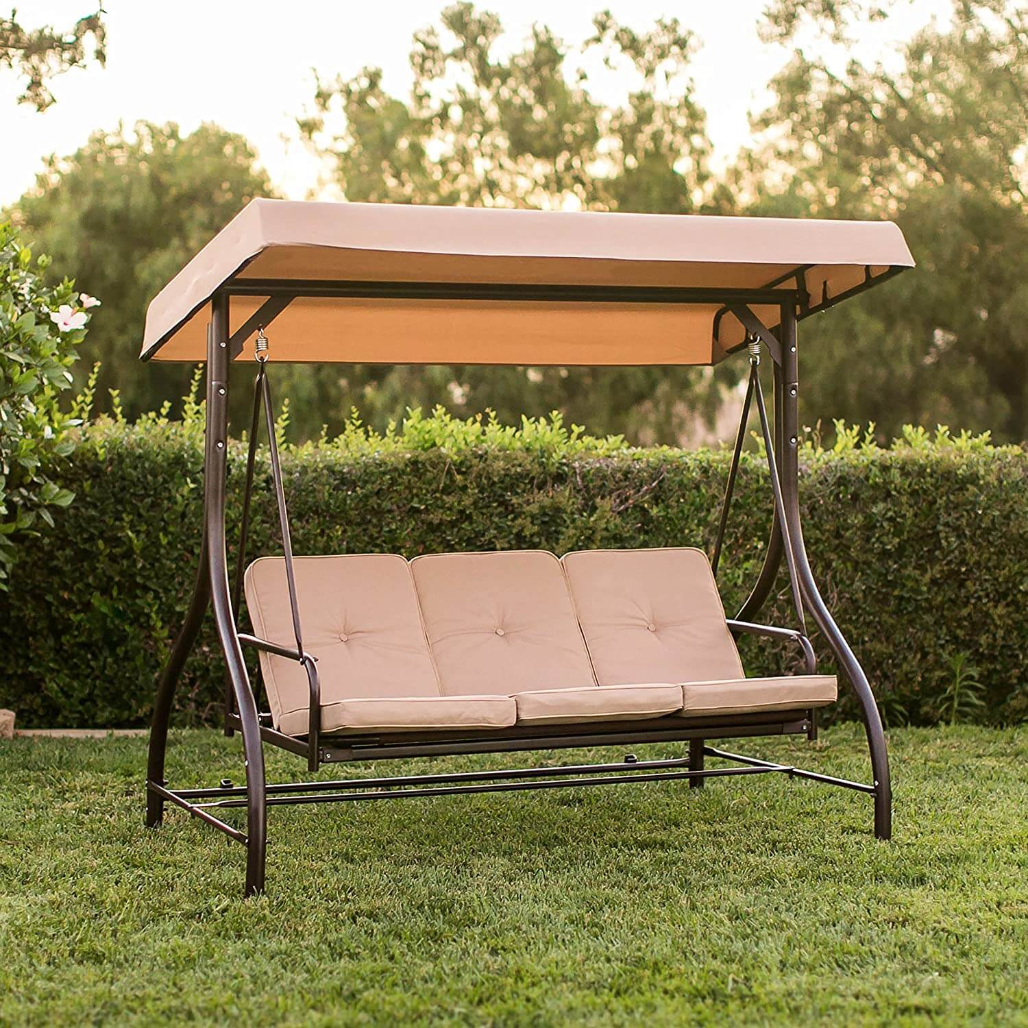 Beige outdoor swing with canopy on a grassy area with trees in the background