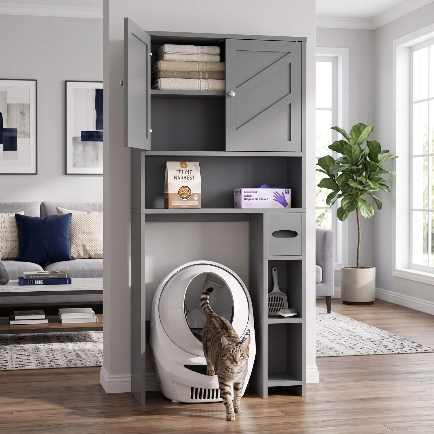 A tall gray over the toilet storage cabinet with open shelving and a lower compartment holding a white automatic litter mat, shown in a bright living room with a cat walking in front of it.