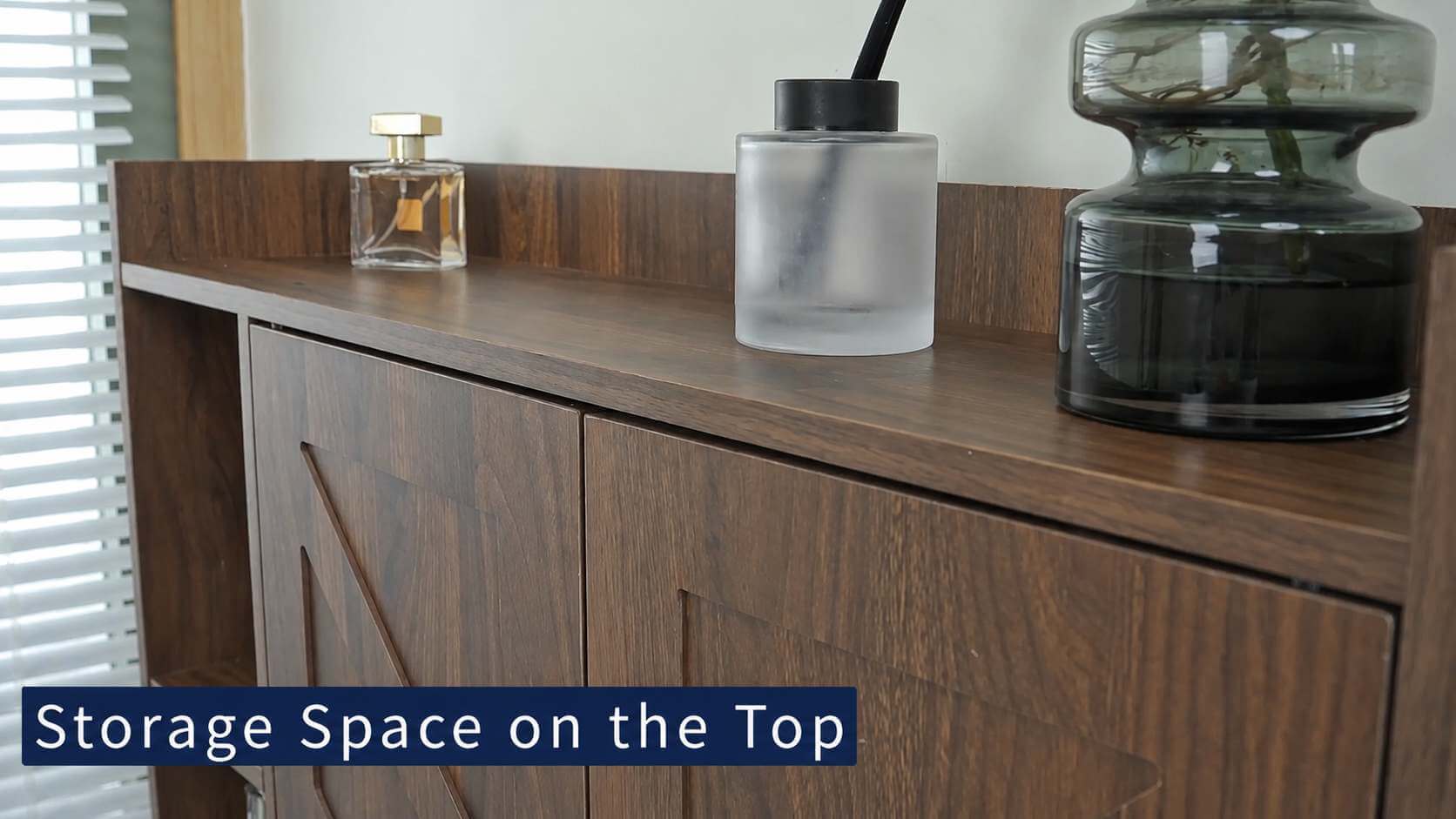 A close-up of a dark brown wooden above the toilet storage cabinets​ with a top surface, showing storage space on top. Decorative items including a frosted glass bottle, a small perfume bottle, and a dark glass vessel are placed on the cabinet.
