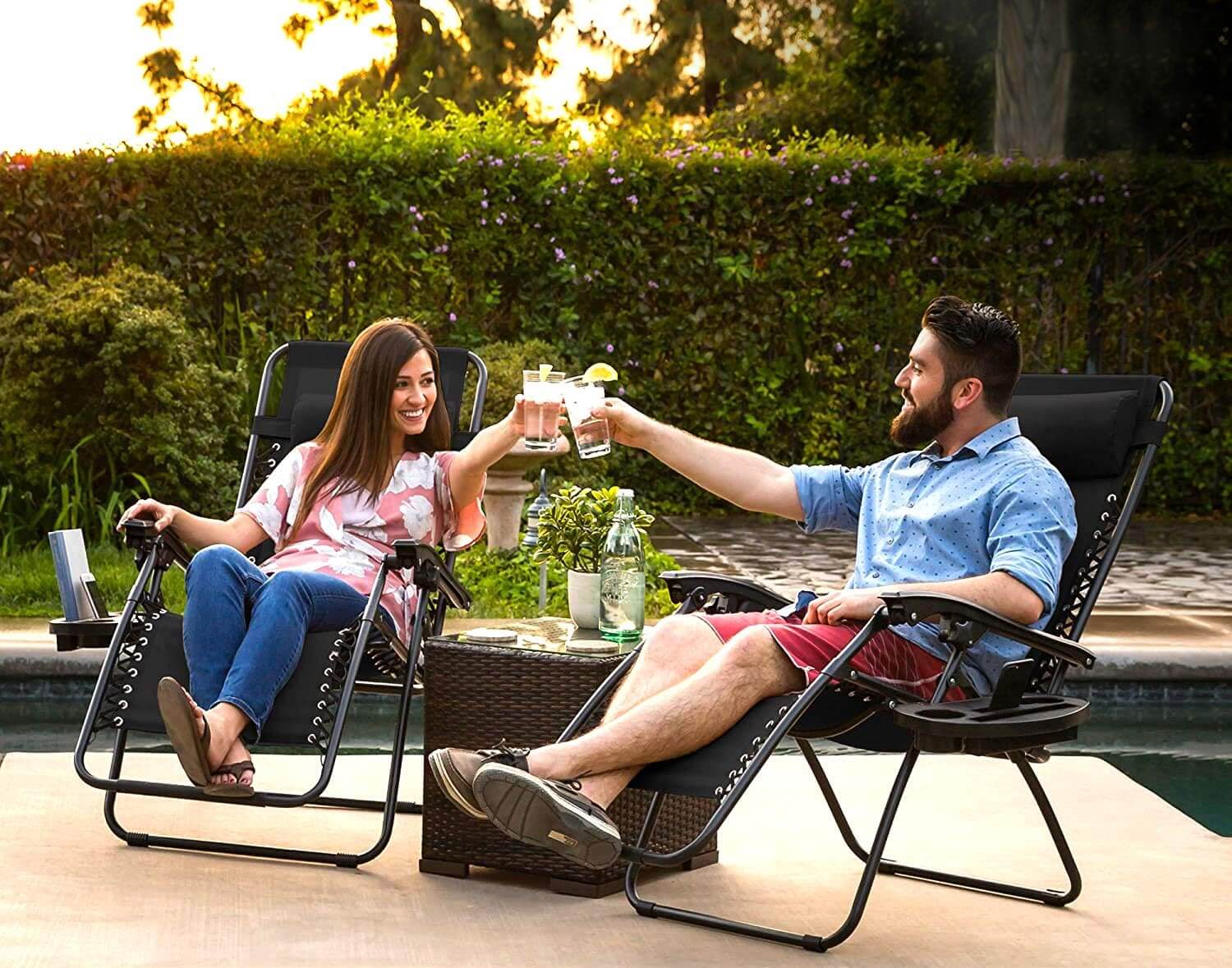 Two people sitting on outdoor patio recliners by a pool, enjoying drinks and conversation.