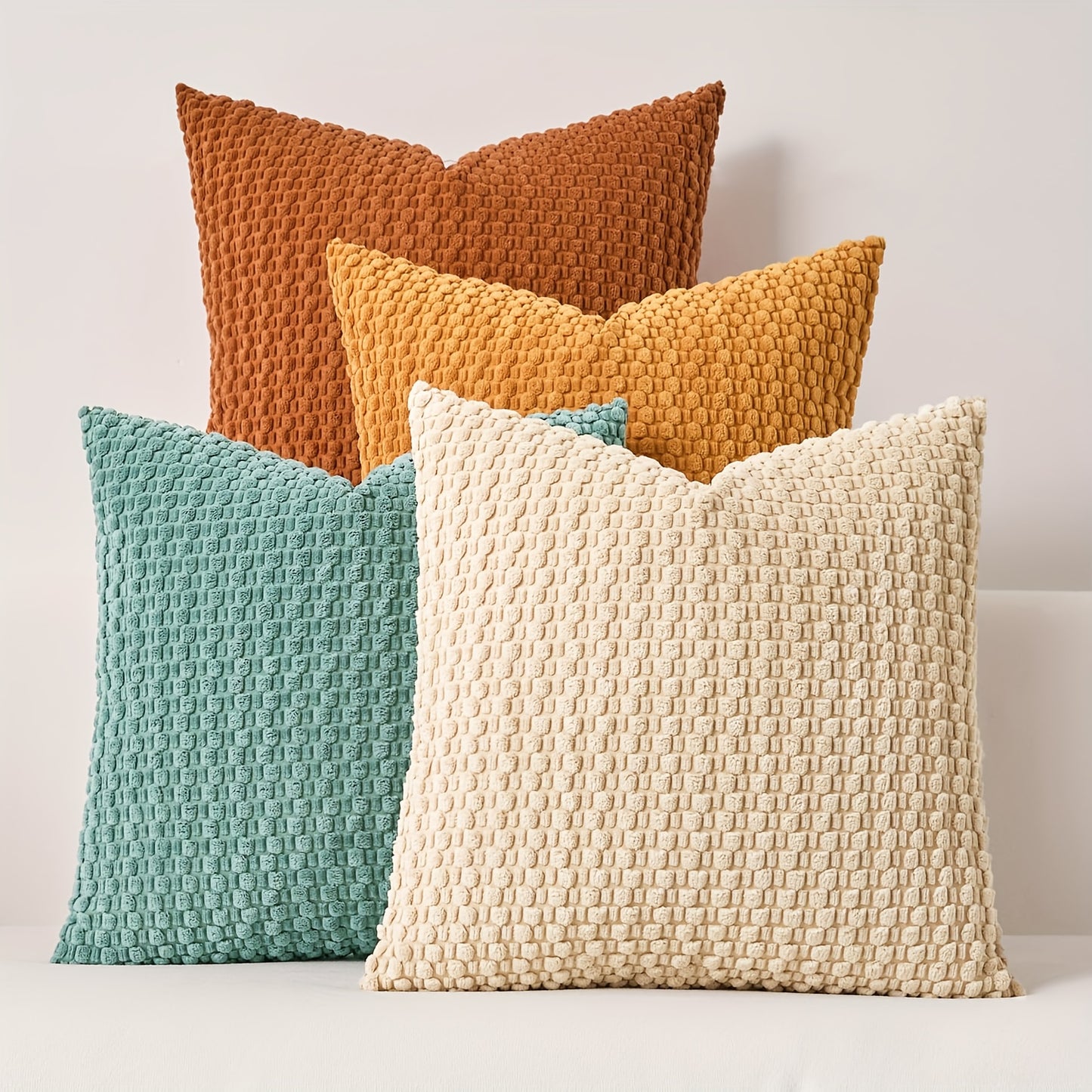 Four textured pillows in brown, yellow, blue, and beige on a light background