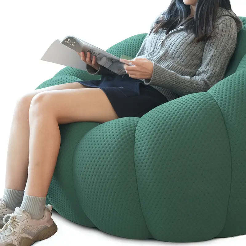 Person sitting on a green bean bag chair reading a magazine.