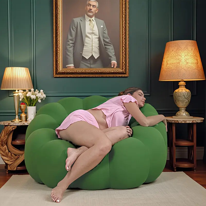 Woman lying on a green bean bag chair in a room with lamps and a framed portrait.