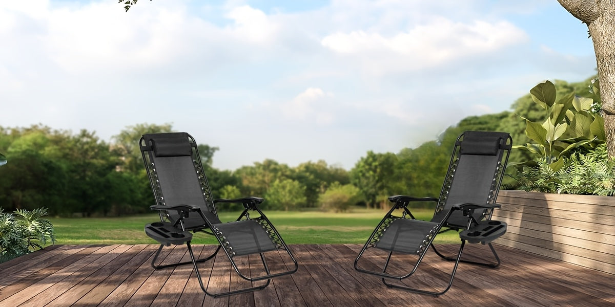 Two black lounge chairs on a wooden deck with a scenic background of trees and sky.