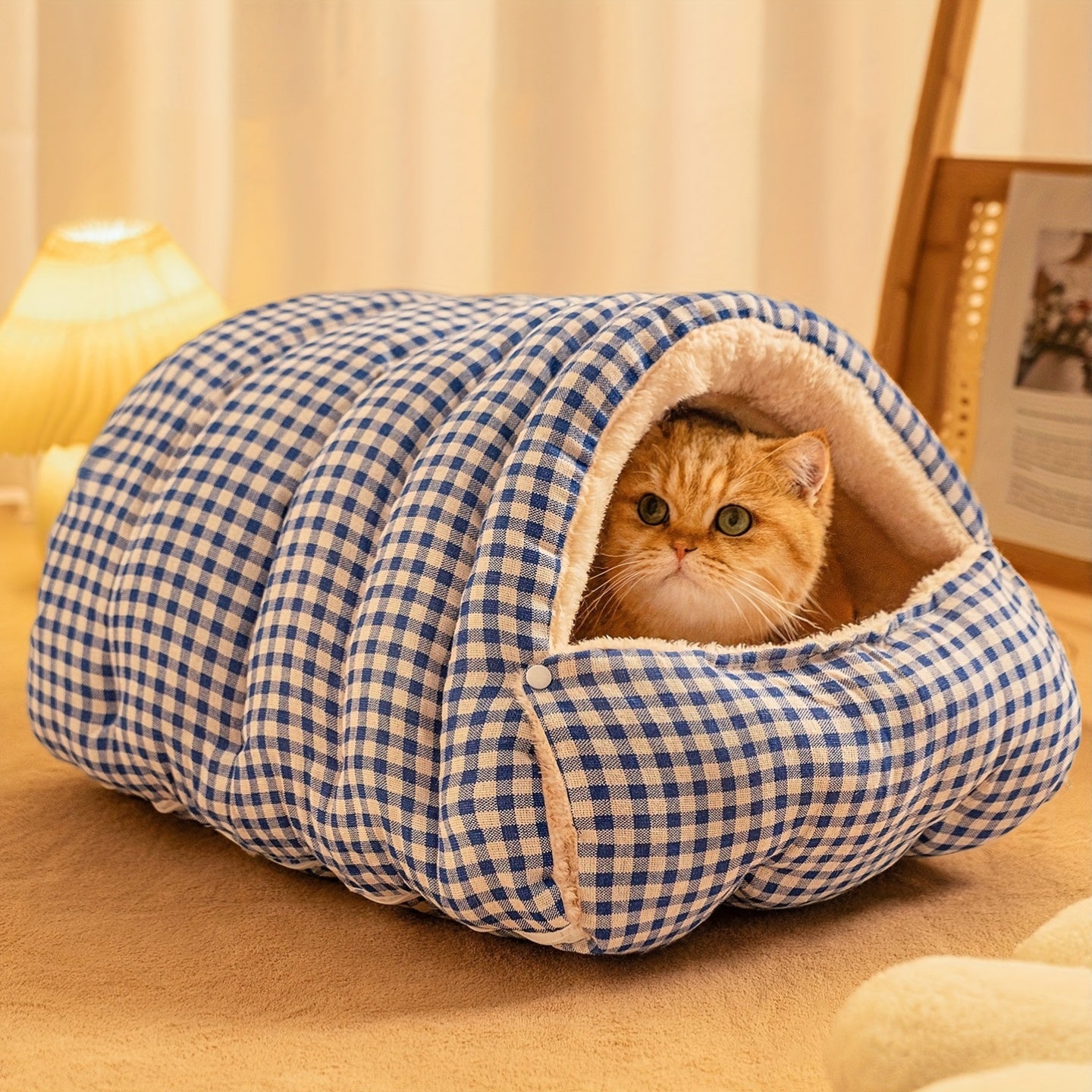 Cat peeking out from a blue and white checkered wool cat cave on a wooden floor.