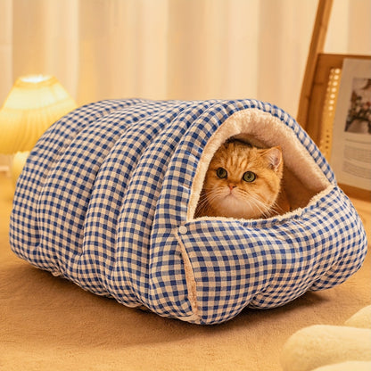 Cat peeking out from a blue and white checkered wool cat cave on a wooden floor.
