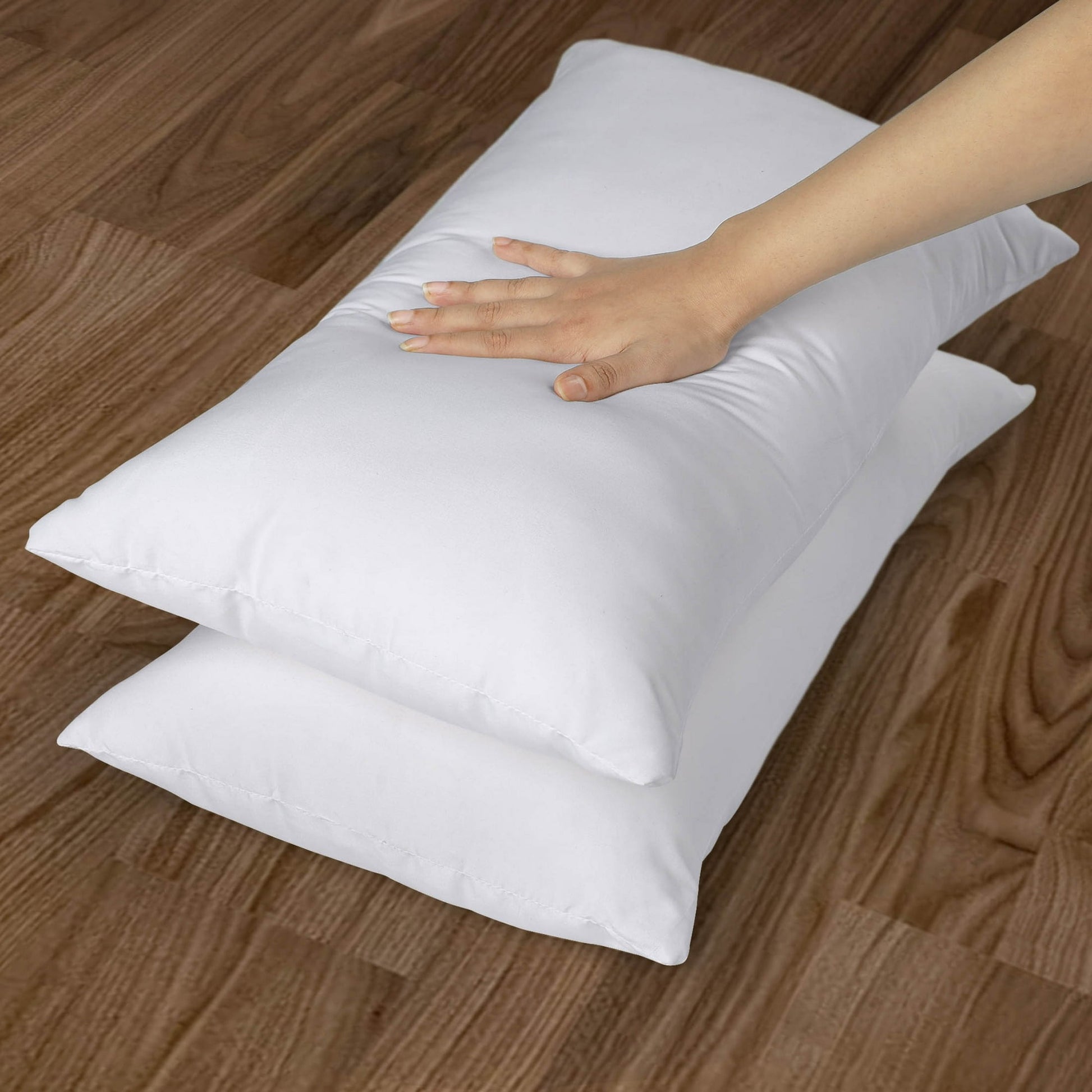 White pillows on a wooden floor with a hand touching one of them.