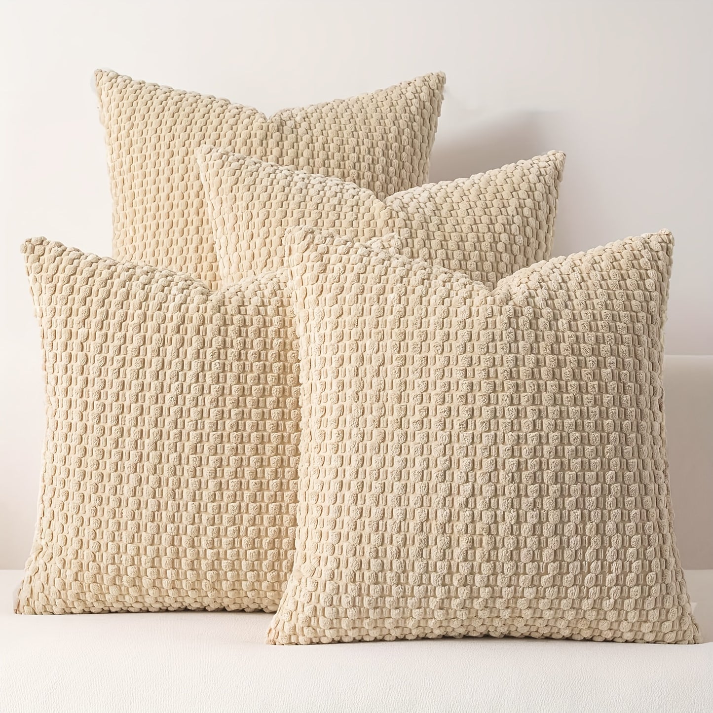 Three beige textured pillows on a white surface with a light gray background