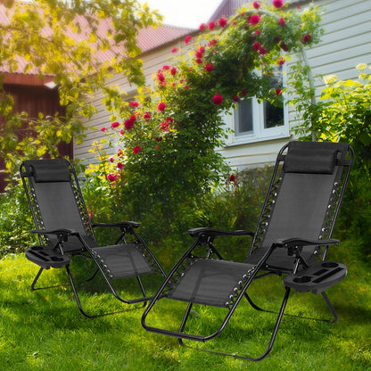 Two black patio chairs on a grassy area with a house and flowers in the background