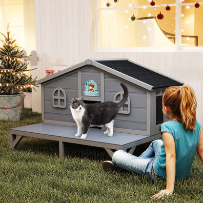 Woman sitting on grass next to a gray cat house with a cat inside, Christmas decorations in the background.