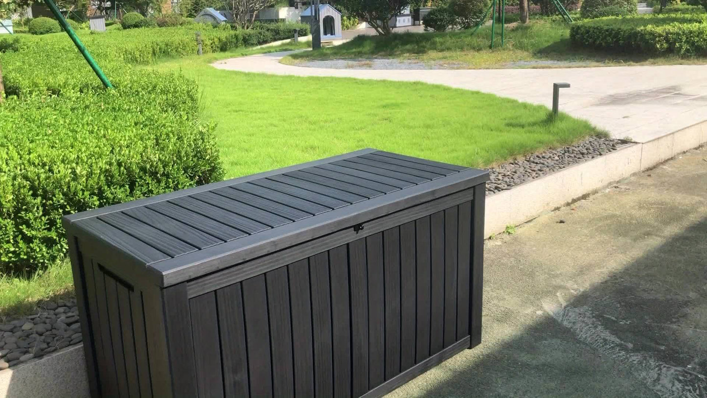 Dark gray outdoor storage box on a concrete surface with green grass and bushes in the background