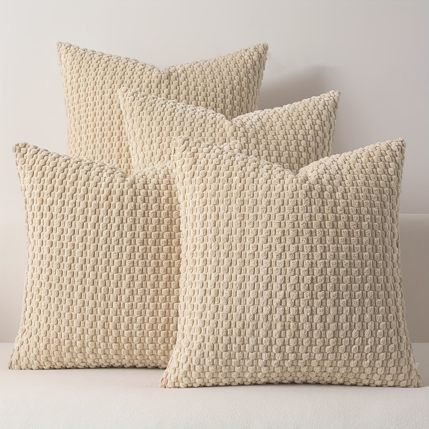 Three textured beige pillows on a white surface with a neutral background